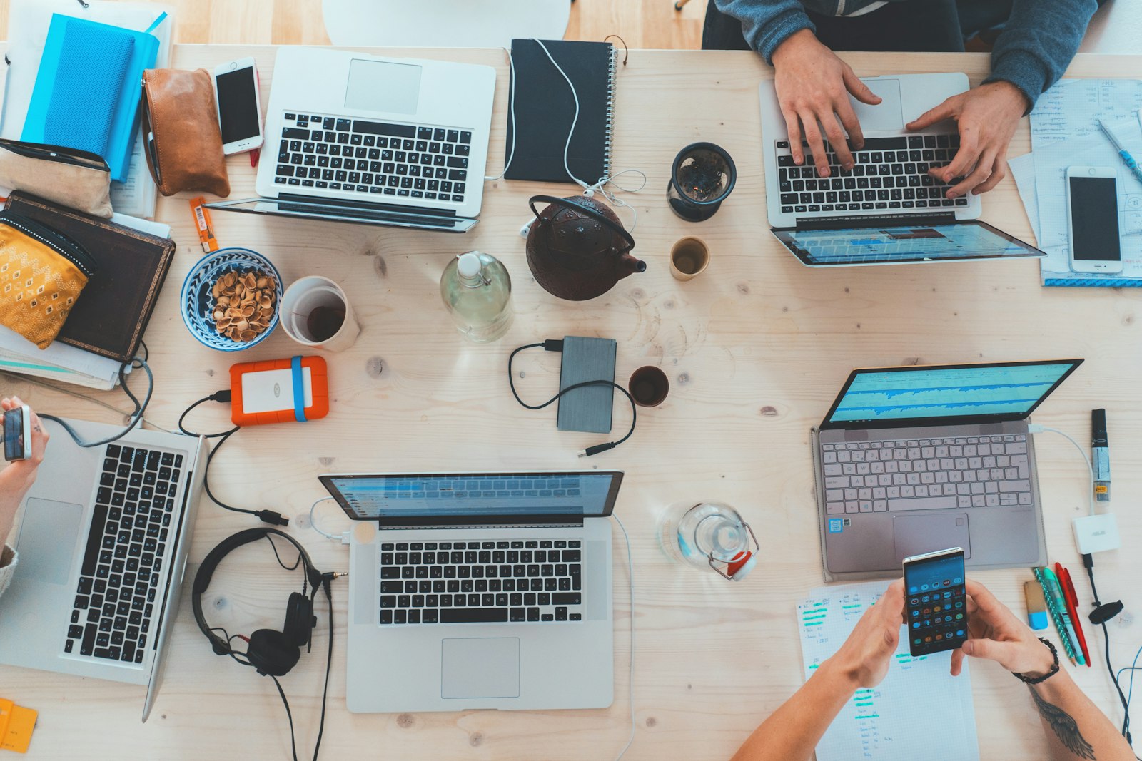 Overhead view of a shared worktable covered with laptops, notebooks and devices