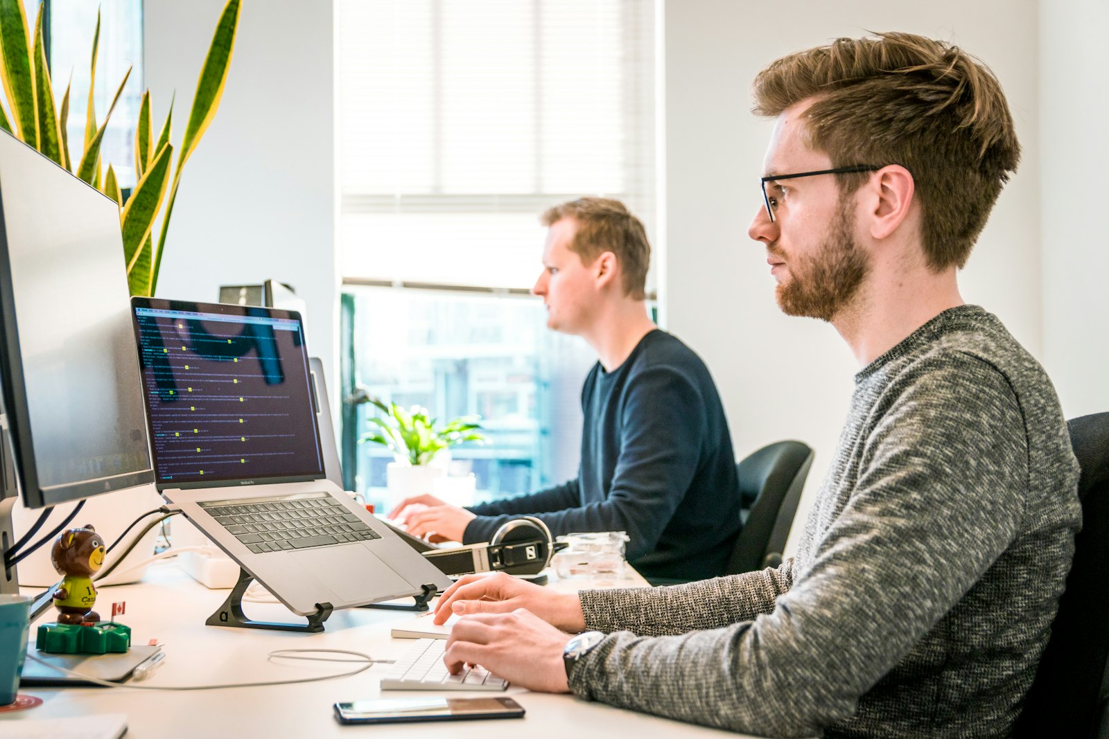 Two engineers working side by side at a desk beside a bright window