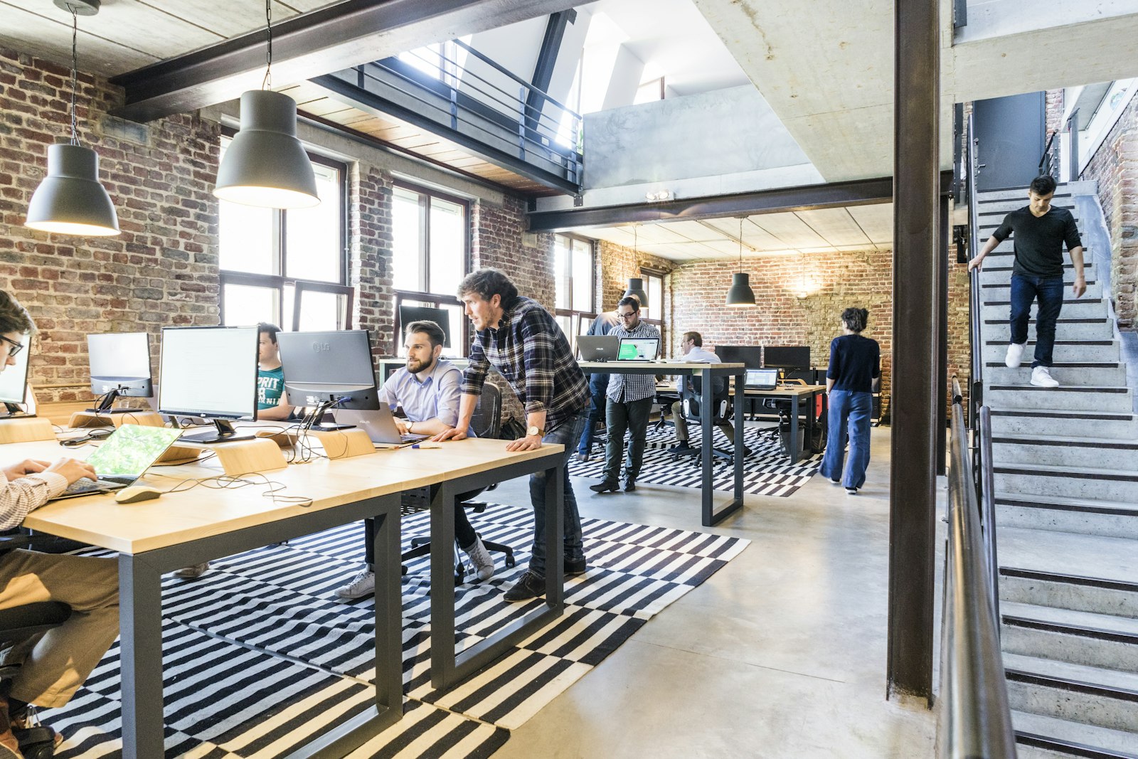 A bright modern office interior with people working at desks near an open staircase